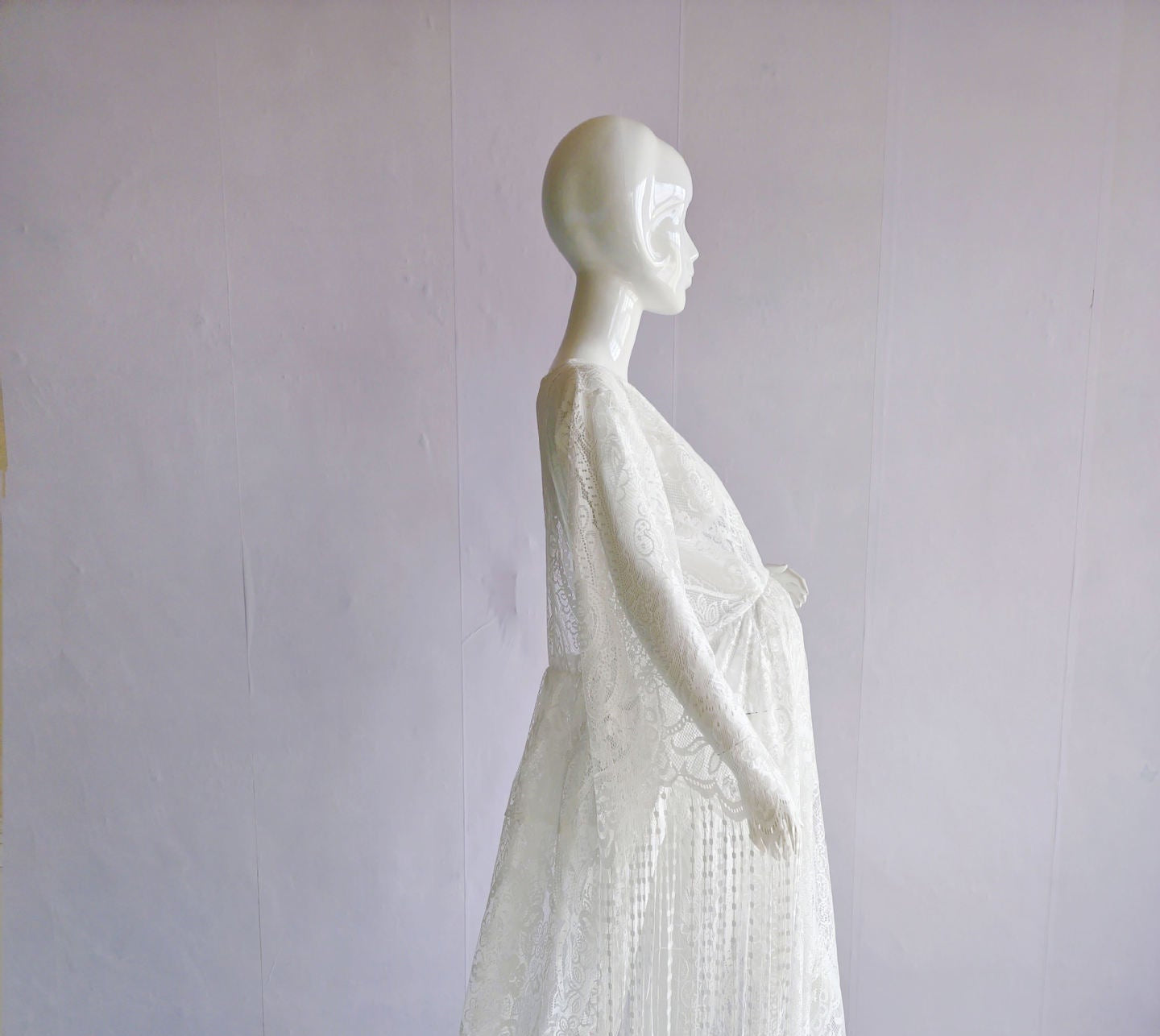Mannequin wearing a white dress with fringe details on a plain background