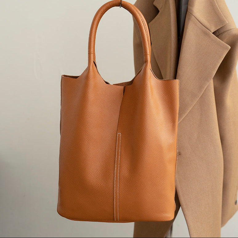 Brown leather tote bag with a beige coat on a light background