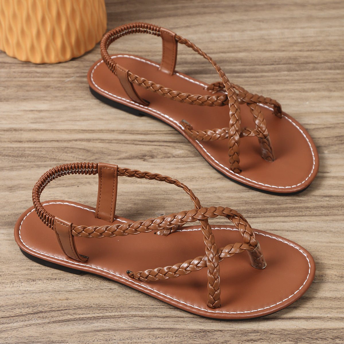 Pair of brown sandals with braided straps on a wooden surface