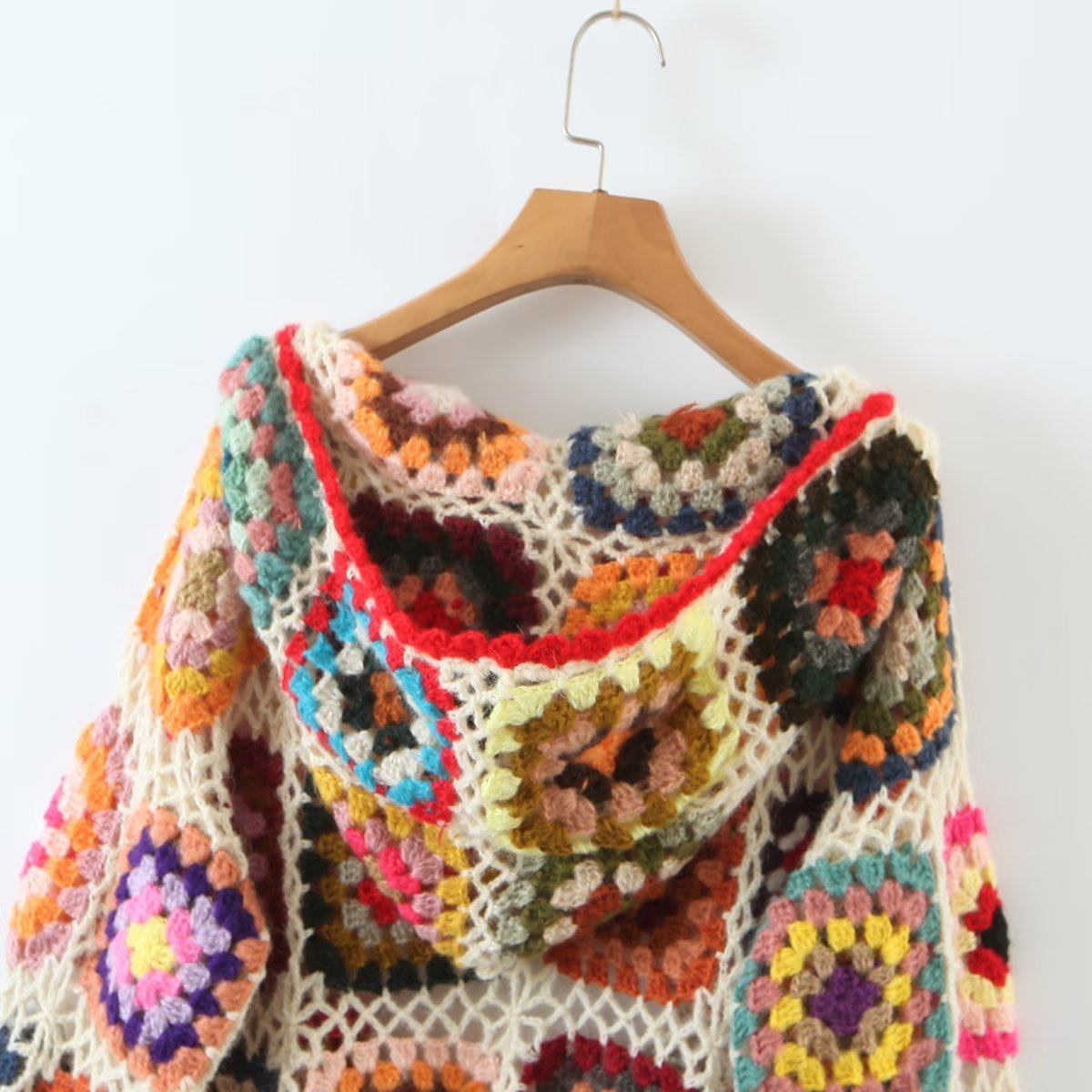 Colorful crocheted shawl on a wooden hanger against a white background