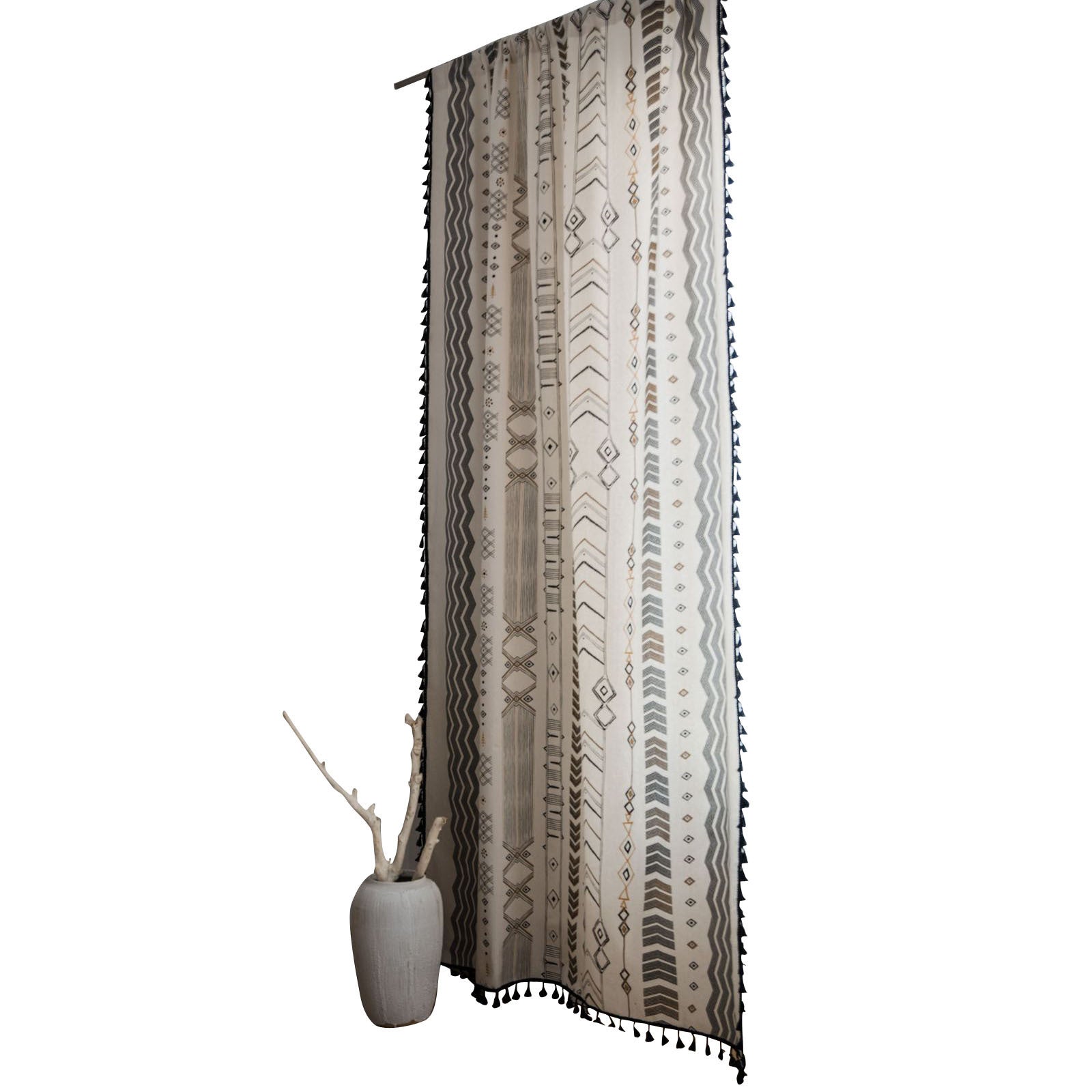 Decorative curtain with tribal pattern and fringe, next to a small vase with branches on a white background