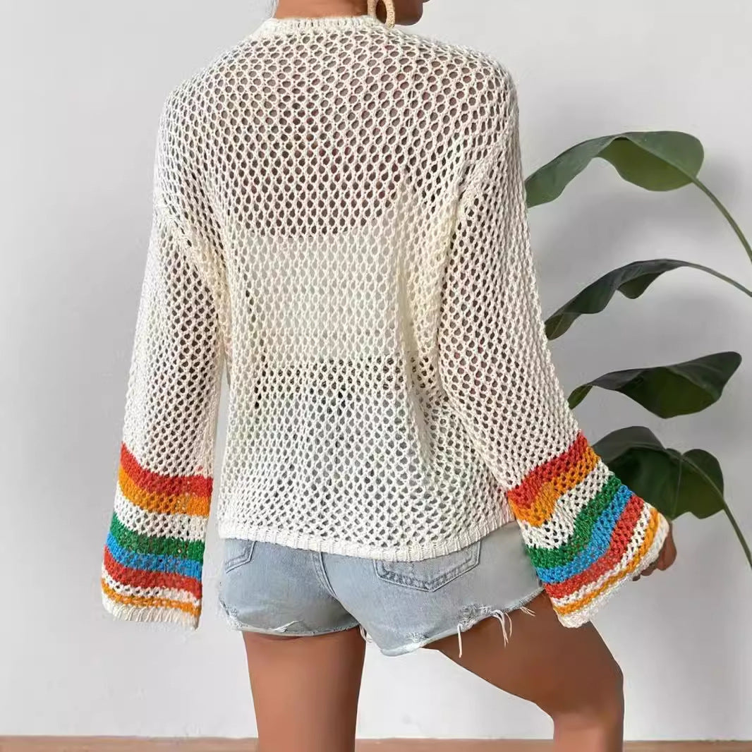 Person wearing a white crochet cardigan with rainbow sleeves against a plain background