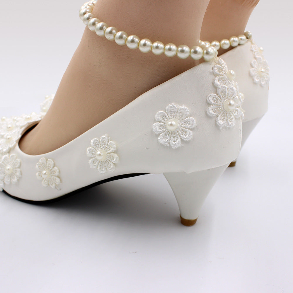 White wedding shoes with floral embellishments and pearl anklets on a white background