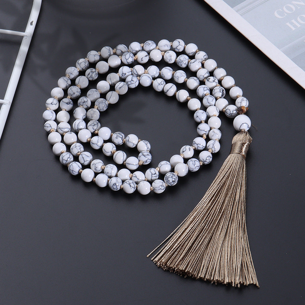 White beaded necklace with a tassel on a dark surface