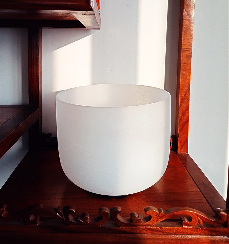 White singing bowl on a wooden surface with a wooden shelf in the background