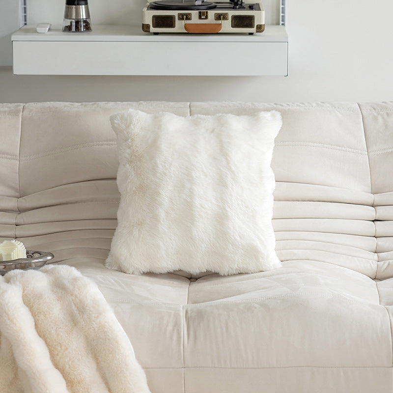 White sofa with a fluffy white pillow and blanket, and a record player on a shelf in the background.
