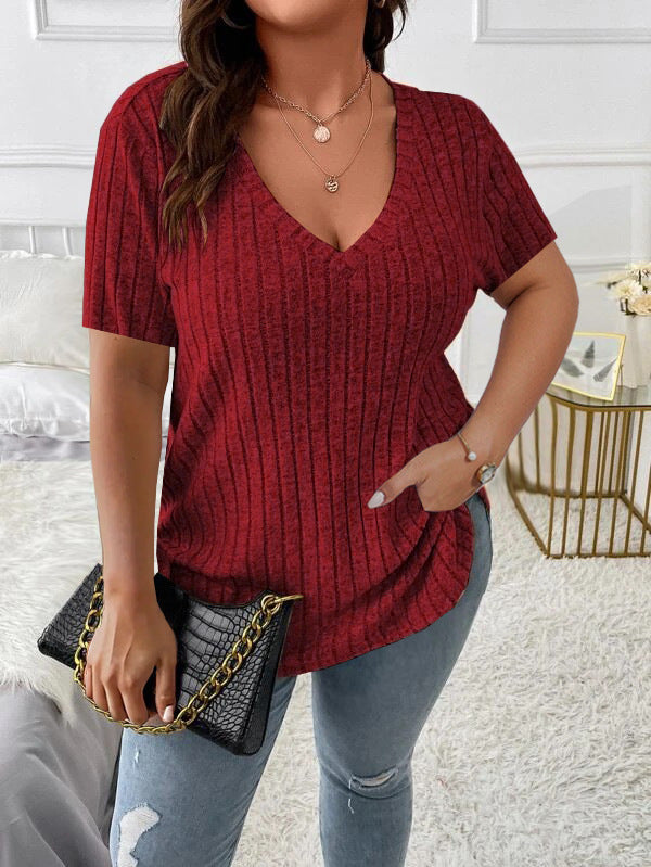 Woman wearing a red textured top and blue jeans, holding a black handbag.