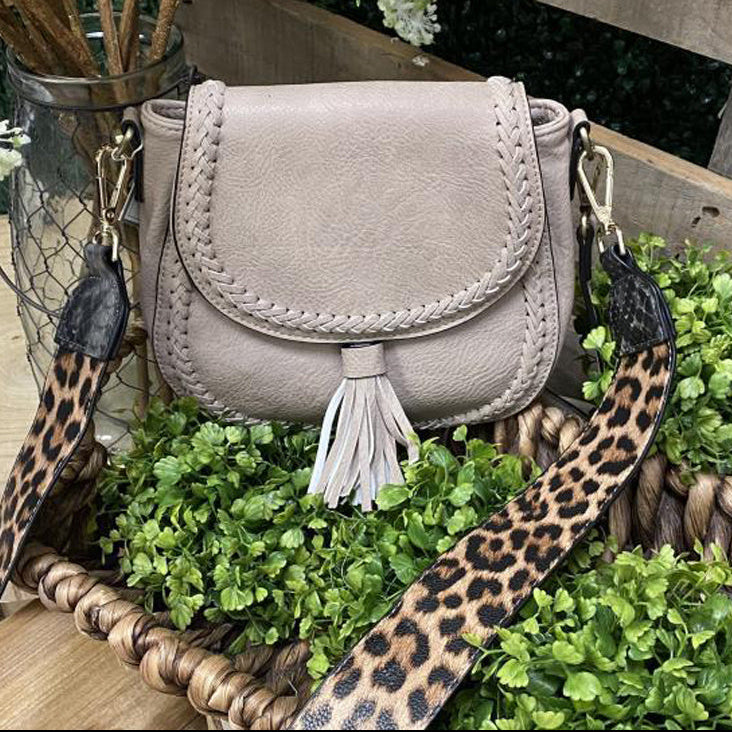 Small beige handbag with a leopard print strap on a green plant background