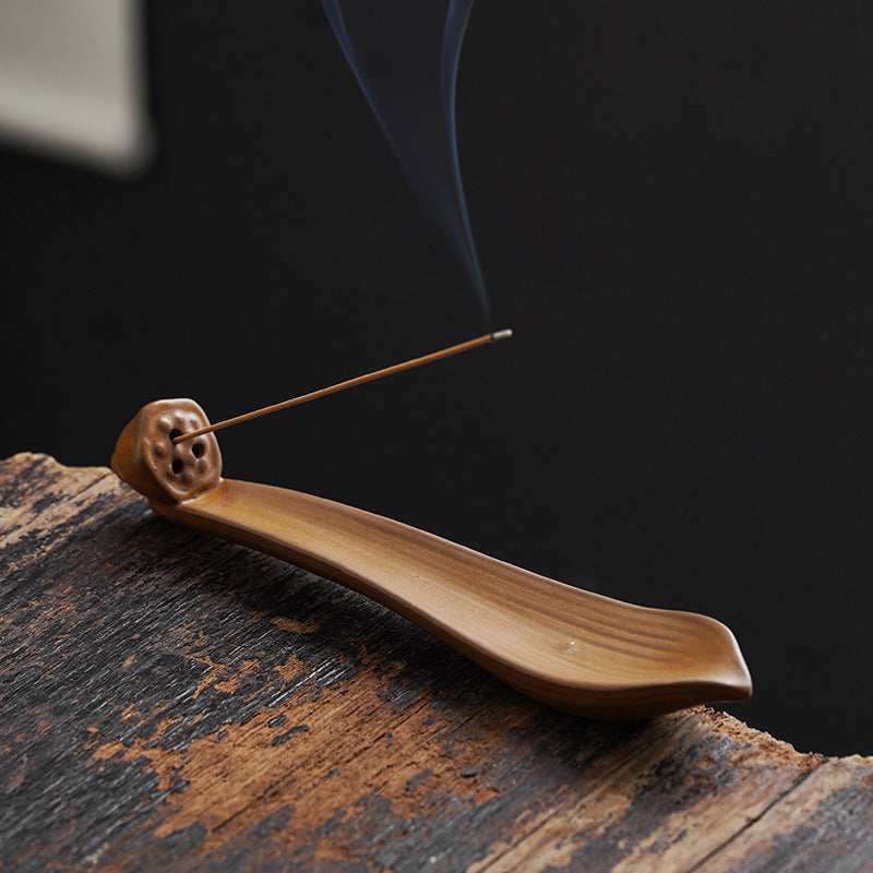 Wooden incense holder with a burning incense stick on a dark background