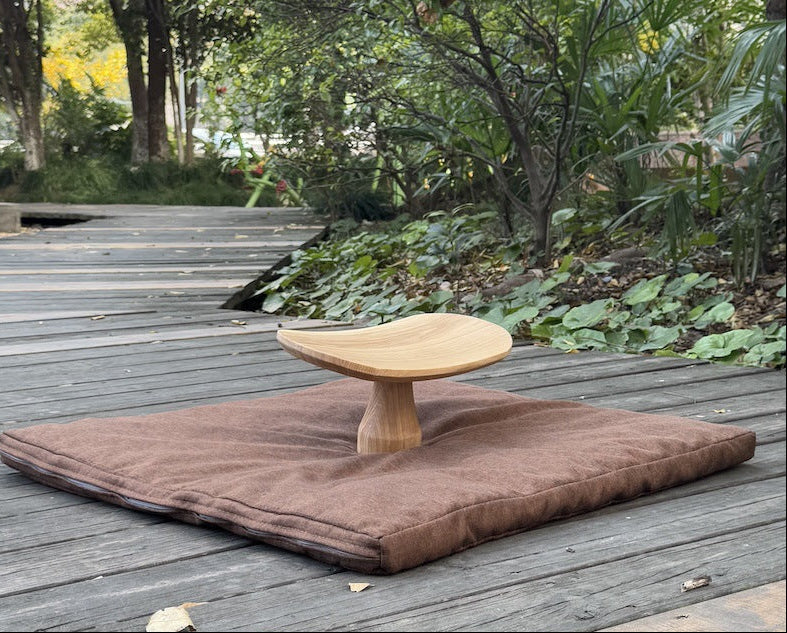 Wooden stool on a brown mat on a wooden deck with greenery in the background