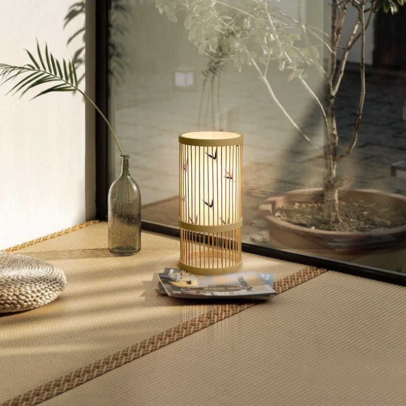 Wooden table lamp on a textured surface with plants and a glass bottle in the background