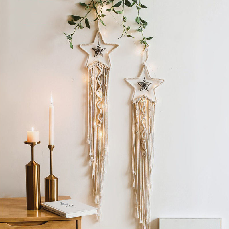 Two star-shaped macrame wall hangings with lights on a white wall, next to candles and a notebook.