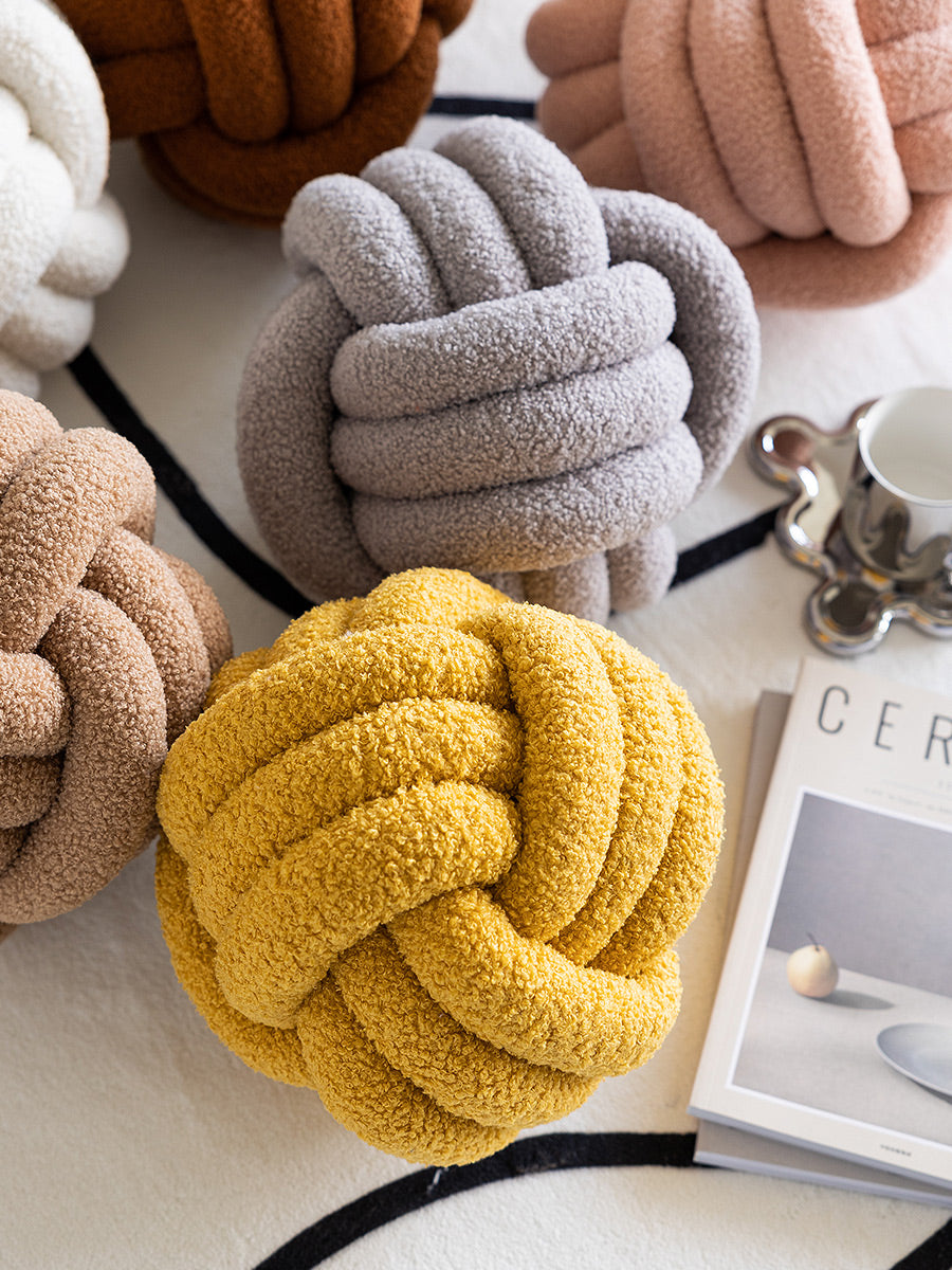 Decorative knot pillows in various colors on a surface with a magazine in the background.