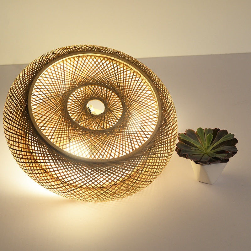 Woven rattan wall light fixture on a neutral background with a small plant.