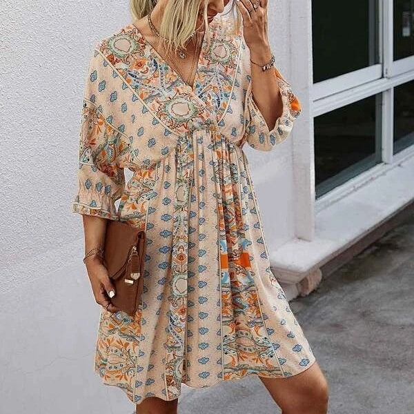 Woman wearing a floral dress holding a brown bag against a white wall.
