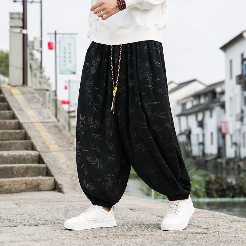 Person wearing black floral-patterned harem pants and white sneakers in an urban setting.