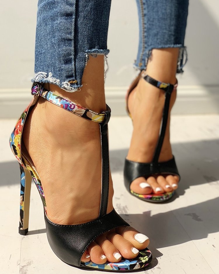 Black high-heeled sandals with colorful straps worn with ripped jeans on a light background