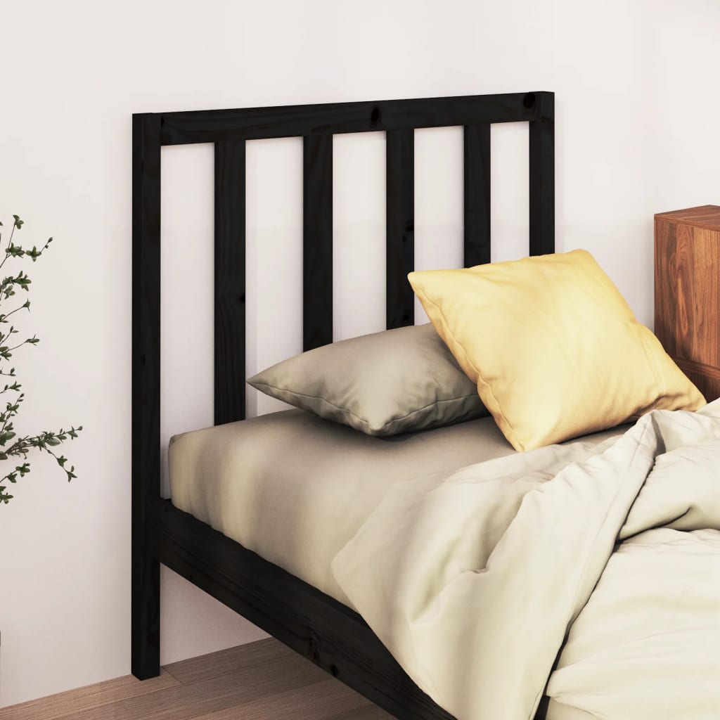 Black wooden headboard with pillows and bedding on a bed against a white wall.