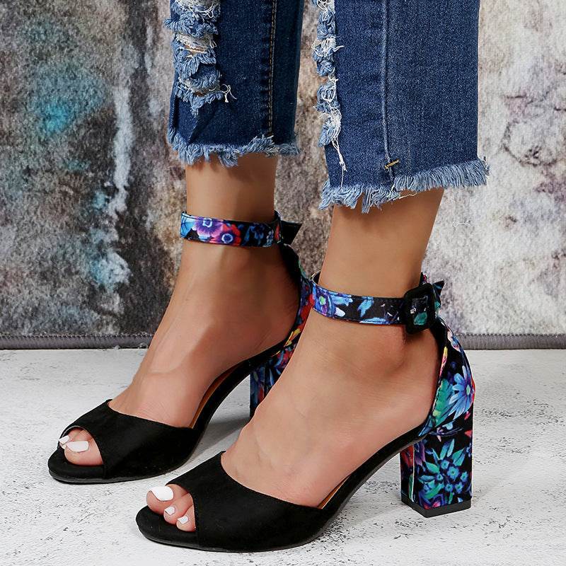 Black open-toe sandals with floral ankle straps worn with denim shorts.