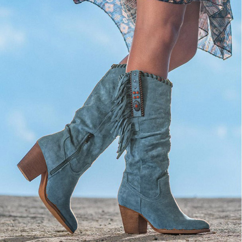 Blue suede knee-high boots with fringe details on a blurred outdoor background