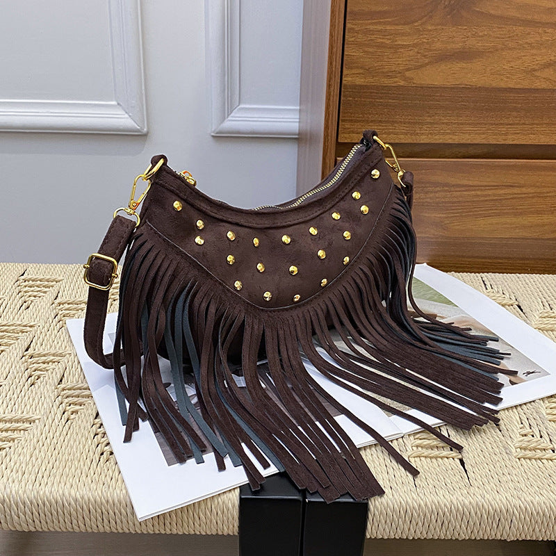 Brown handbag with gold studs and fringes on a textured surface.