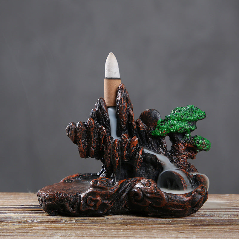 Decorative incense burner with mountain and tree design on a wooden surface