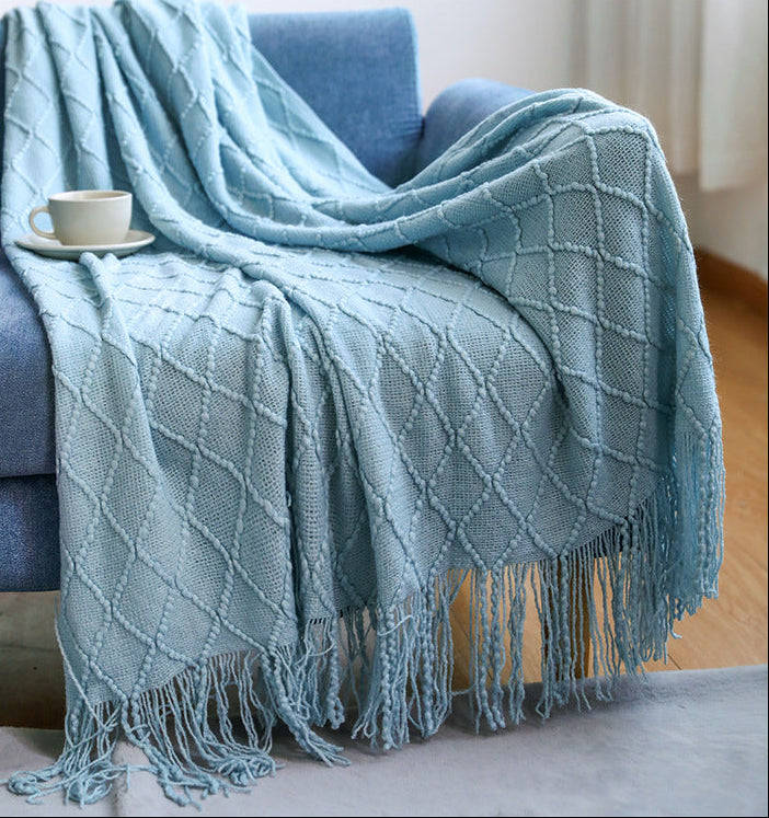 Light blue throw blanket draped over a blue sofa with a cup on a small table.