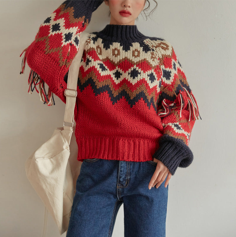 Person wearing a red and black patterned sweater with tassels, holding a beige bag.