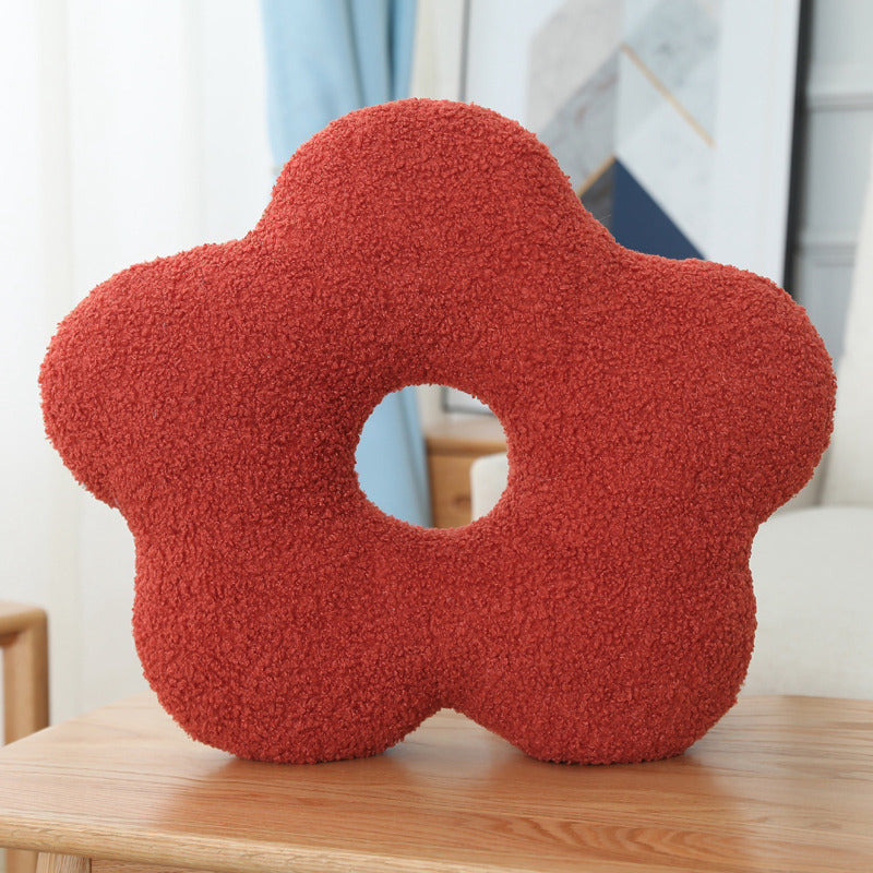 Red flower-shaped pillow on a wooden surface with a blurred indoor background