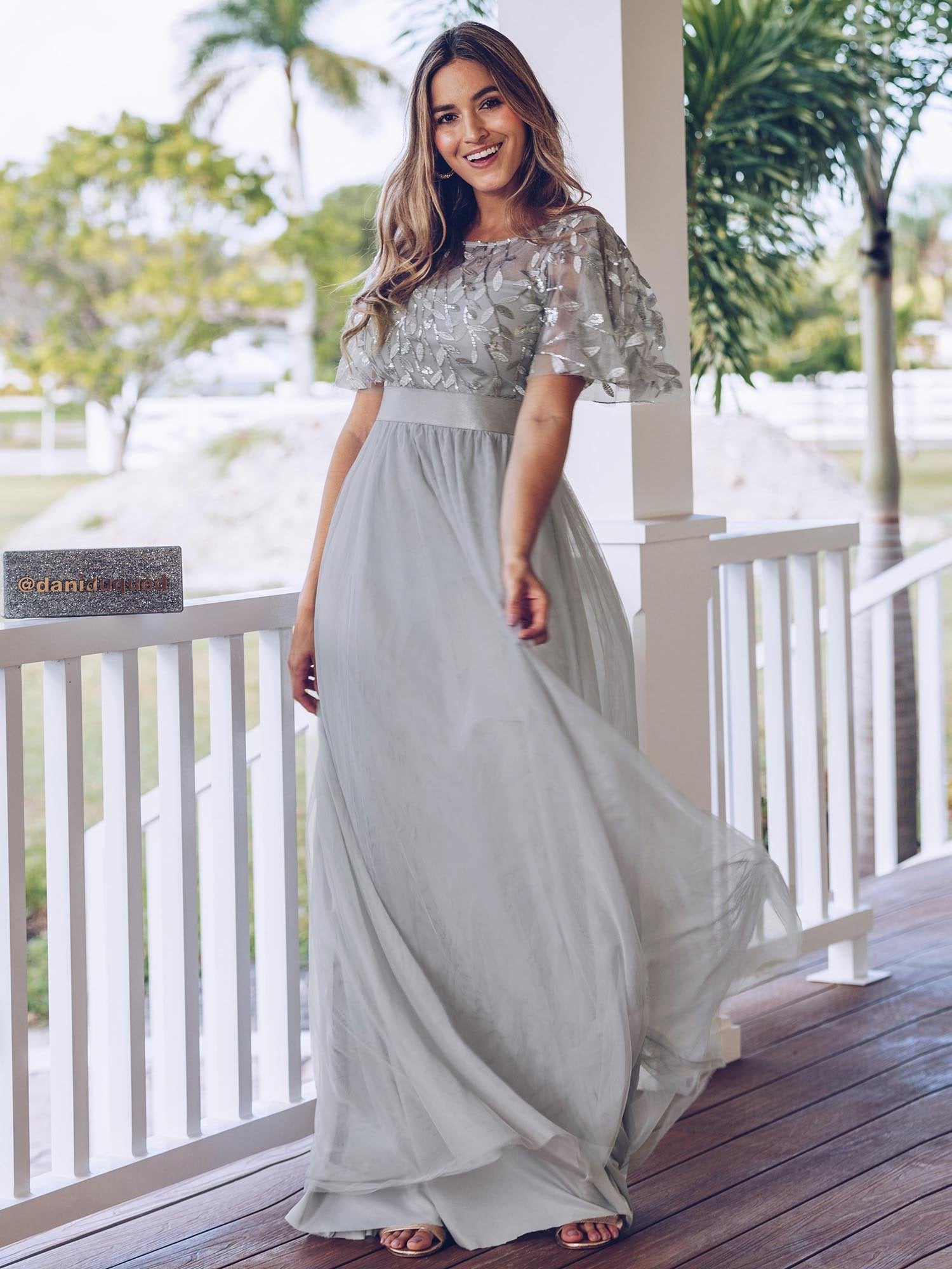Woman in a silver dress standing on a wooden deck with greenery in the background
