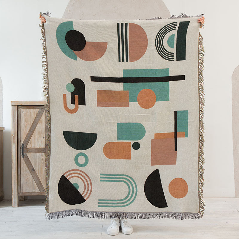 Geometric patterned throw blanket held by a person in a minimalistic room.