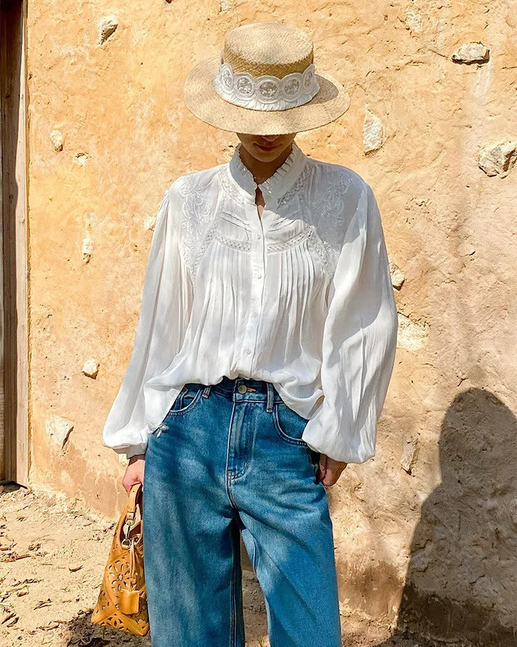 Person wearing a white blouse, blue jeans, and a straw hat against a stone wall.