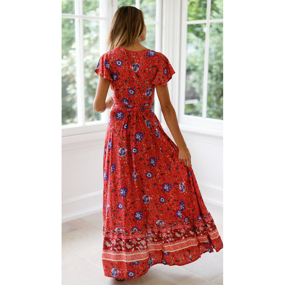 Woman wearing a red floral dress standing in a bright room with large windows.