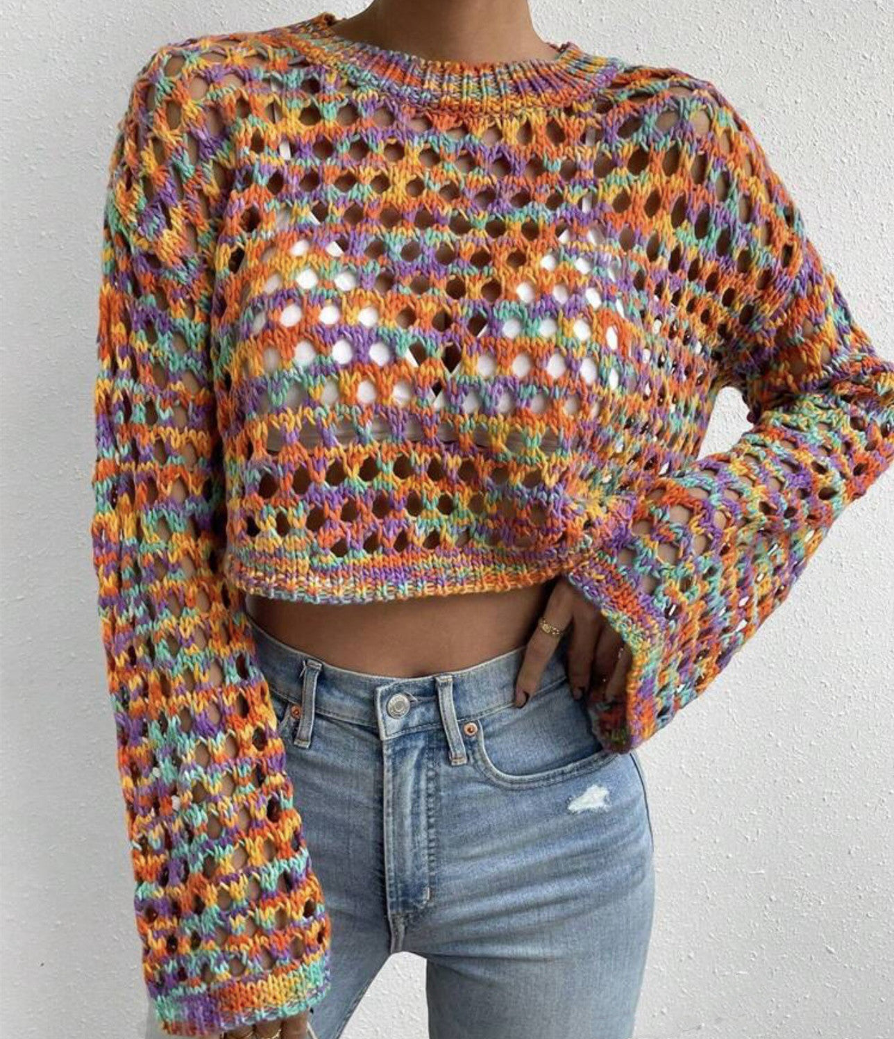 Person wearing a colorful crochet sweater and blue jeans against a white background