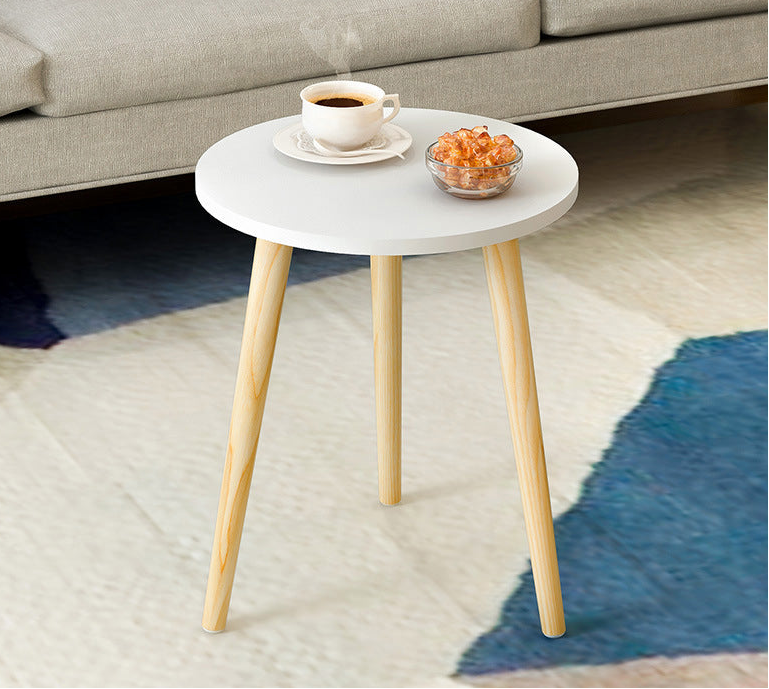 Small round table with white top and wooden legs in front of a sofa.