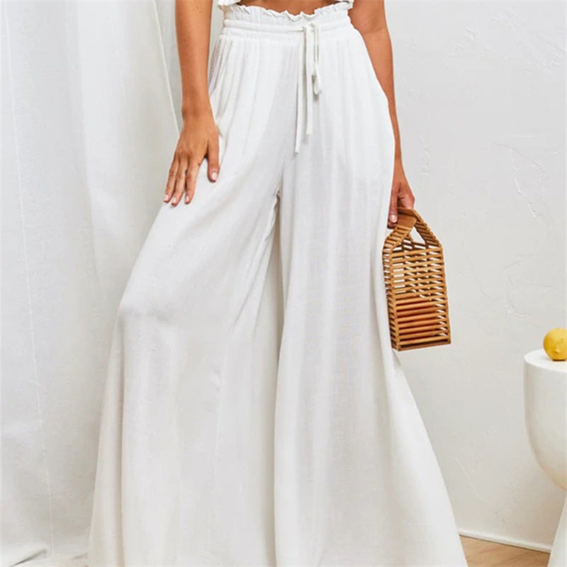 Person wearing white wide-leg pants holding a woven handbag against a plain background