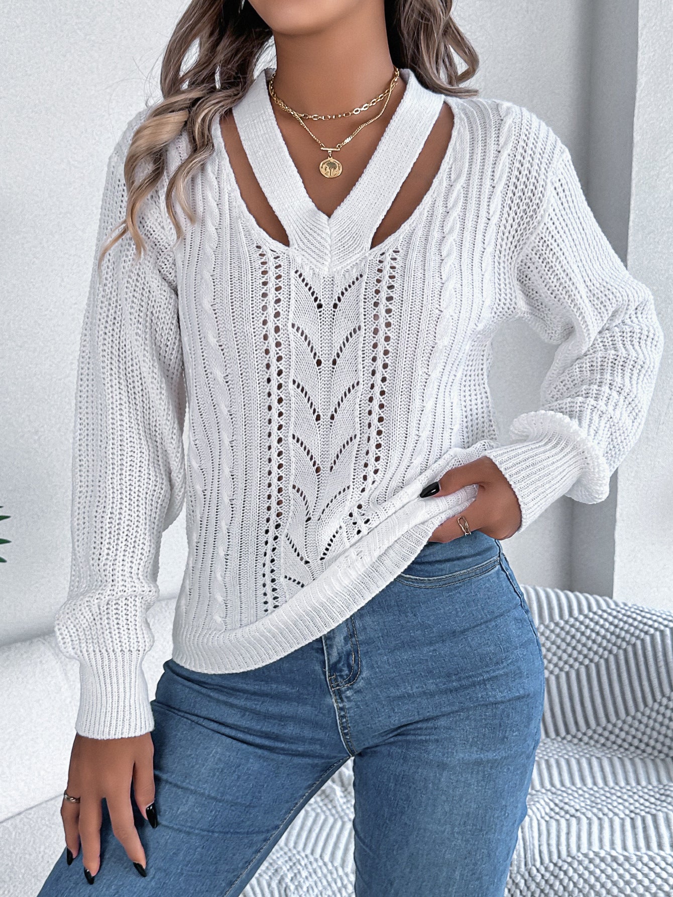 Person wearing a white cable knit sweater and blue jeans indoors.